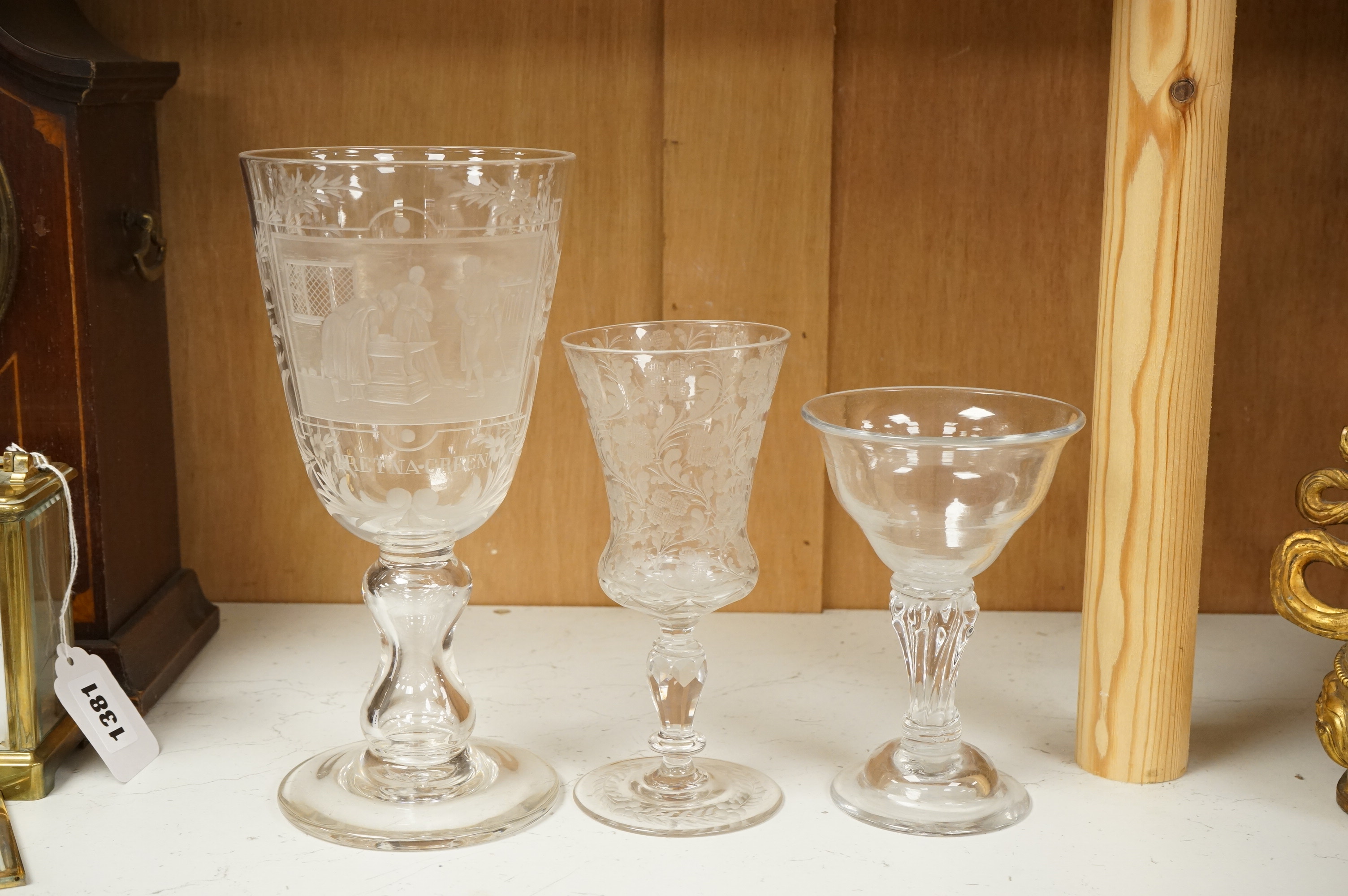 An 18th century sweetmeat glass, a 19th century large wheel engraved ‘Gretna Green’ goblet and a smaller floral engraved glass, tallest 23cm